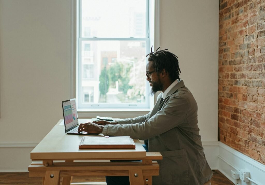 A freelancer sits working on spreadsheets on their laptop at a table, side profile