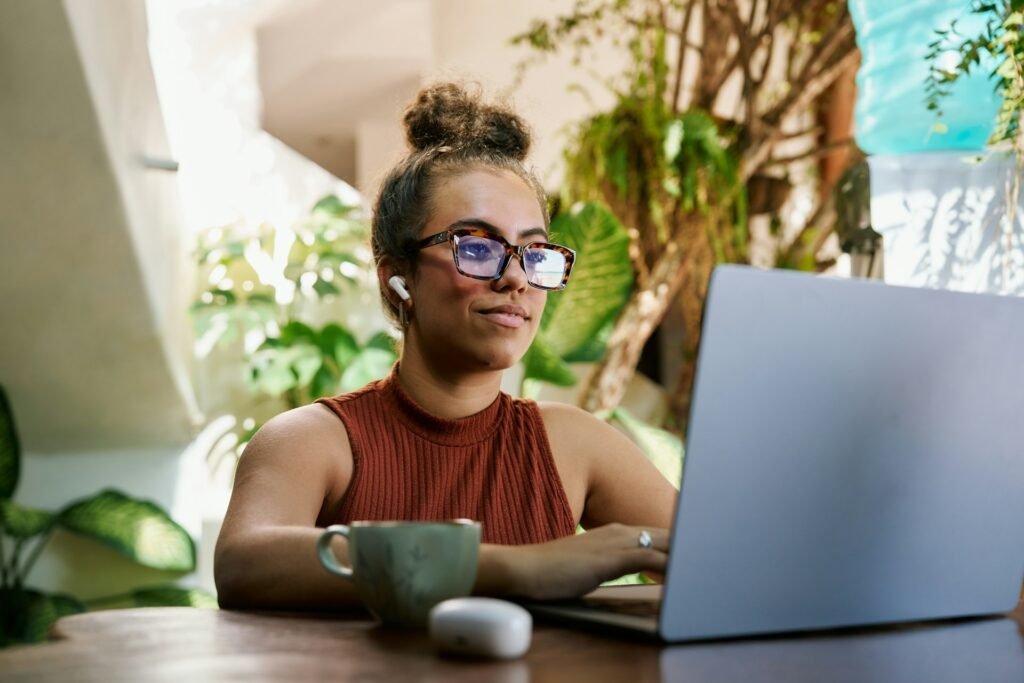 A female freelancer sits on her laptop, with AirPods in, searching for the best project management software for freelancers.