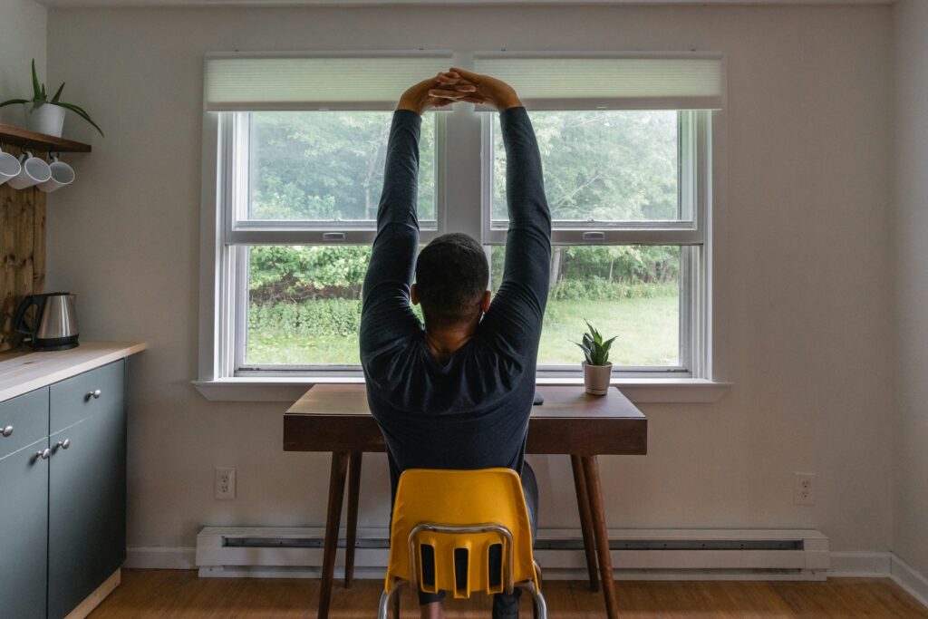 A male freelancer works in his kitchen, stretching his arms above him after finding the best invoicing tool for freelancers