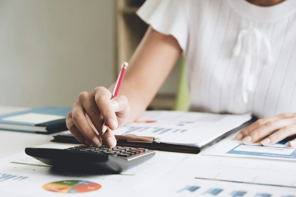 A close-up of a self-employed woman with spreadsheets and documents, working out math on her calculator