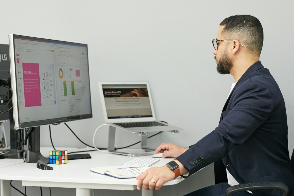 Digital marketing professional working at a dual-monitor setup displaying SEO analytics and a website design. Desktop Accounting Software Without a Subscription is loaded in the background.