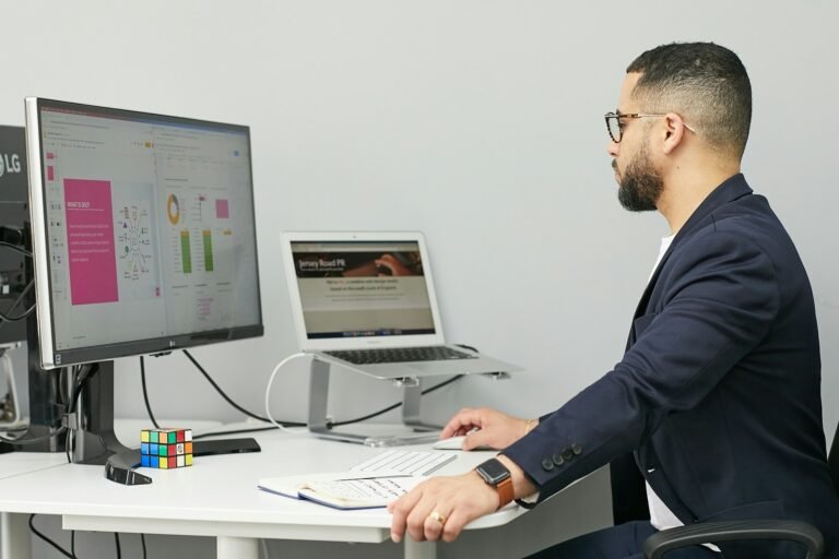 Digital marketing professional working at a dual-monitor setup displaying SEO analytics and a website design. Desktop Accounting Software Without a Subscription is loaded in the background.