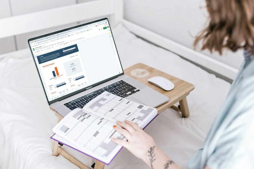 A female freelancer working in bed on her monthly budget on Google Sheets with a diary planner in front of her