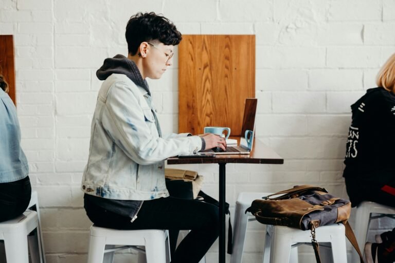 Freelance designer using project management and invoicing software on a laptop in a cafe setting