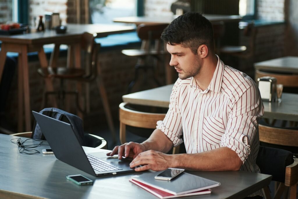 Freelancer learning how to manage freelance projects with clients on a laptop at a café table with a notebook and phone