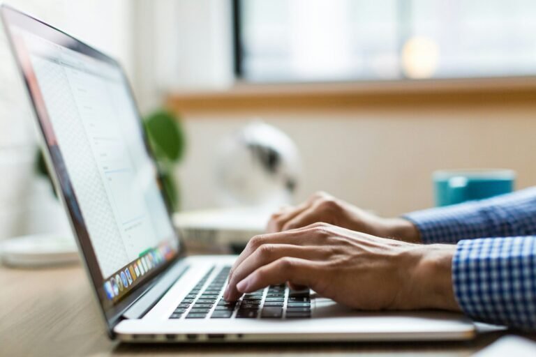 Close-up of a freelancer typing on a MacBook at a desk, looking for the best invoice email sample