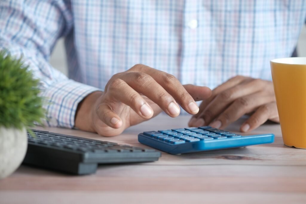 Close-up of a freelancer using a calculator at a desk with a keyboard and coffee mug