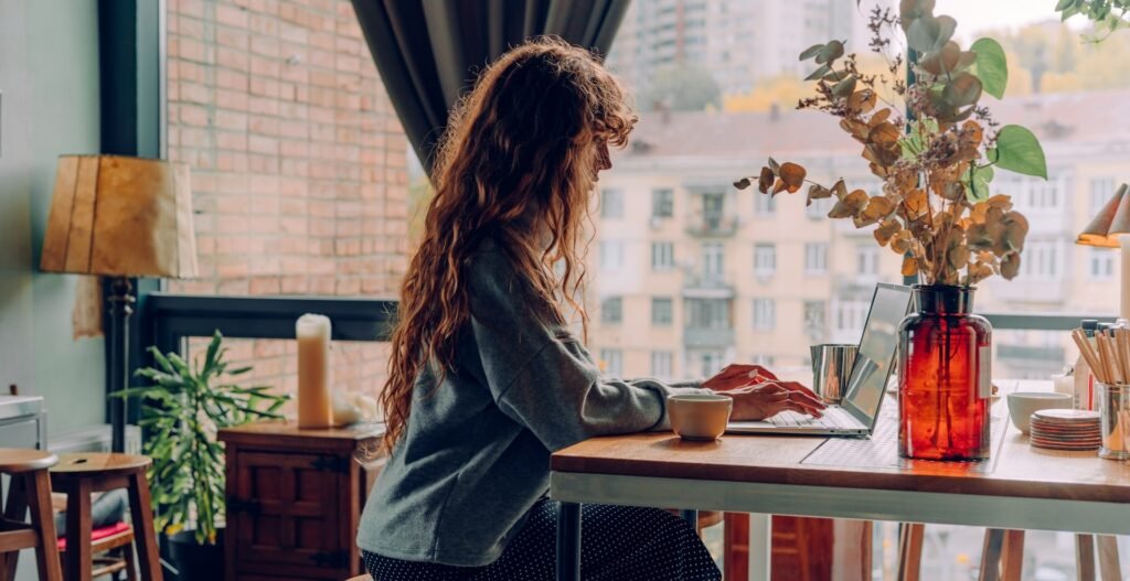Freelancer working on a laptop with a coffee at a cosy café table by a window