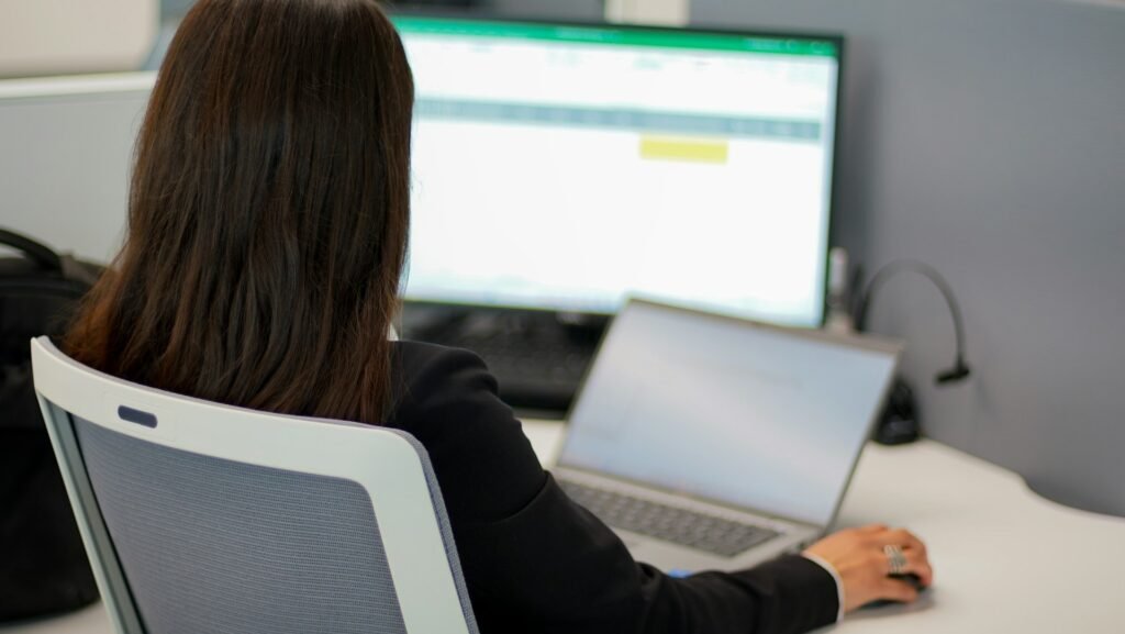 Freelancer working at a desk with a laptop and monitor displaying a spreadsheet application