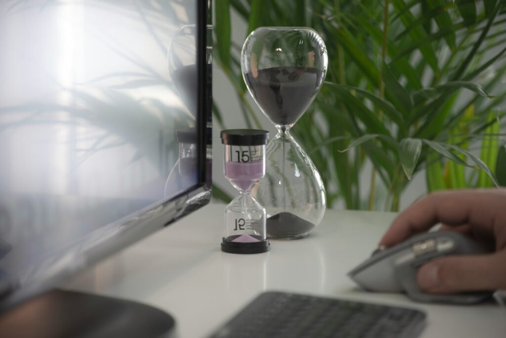 Hourglass timers on a desk next to a monitor and mouse representing time management for freelancers