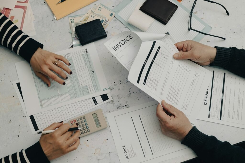 Two people reviewing printed invoices and tax forms with a calculator on a desk