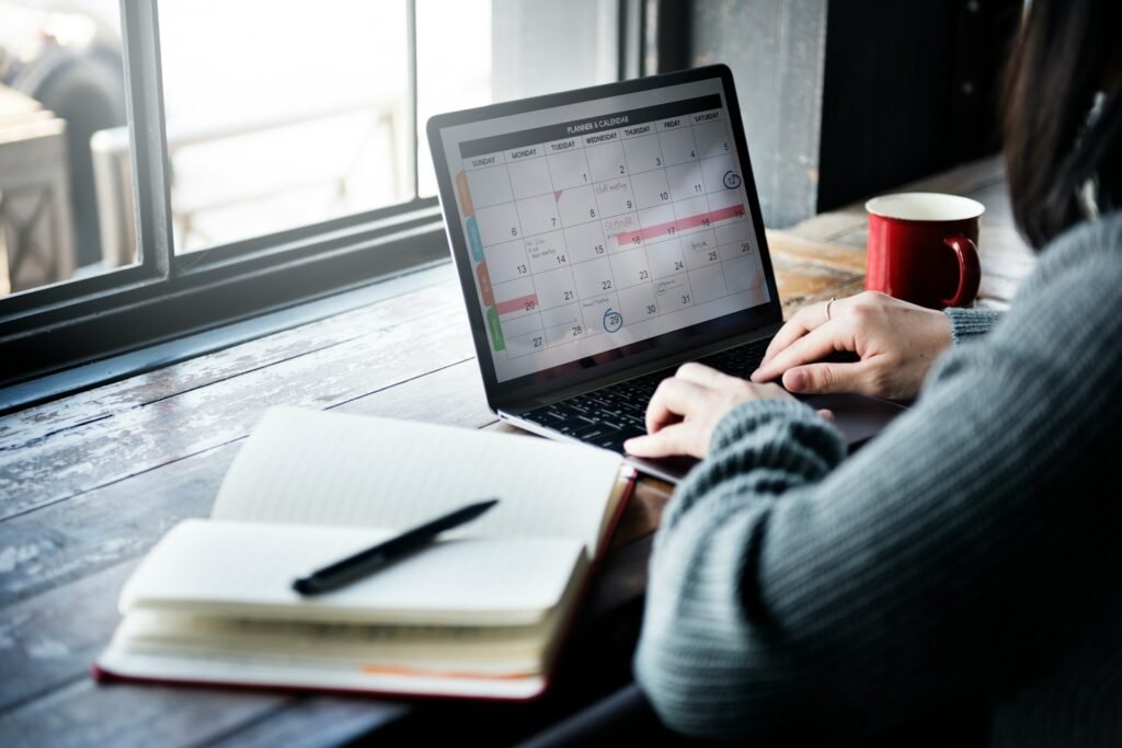 A female freelancer timeblocks her week with a notebook and a calendar open on her computer