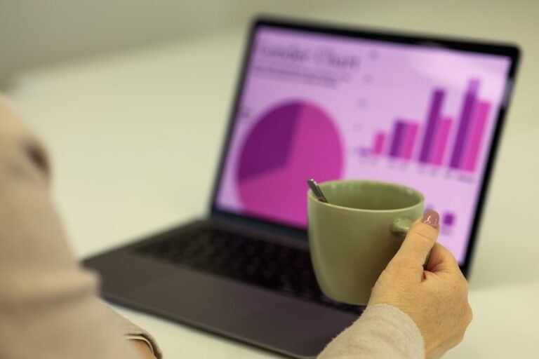 A person holding a coffee cup while looking at a laptop screen showing colorful financial charts of some finance automations tools.