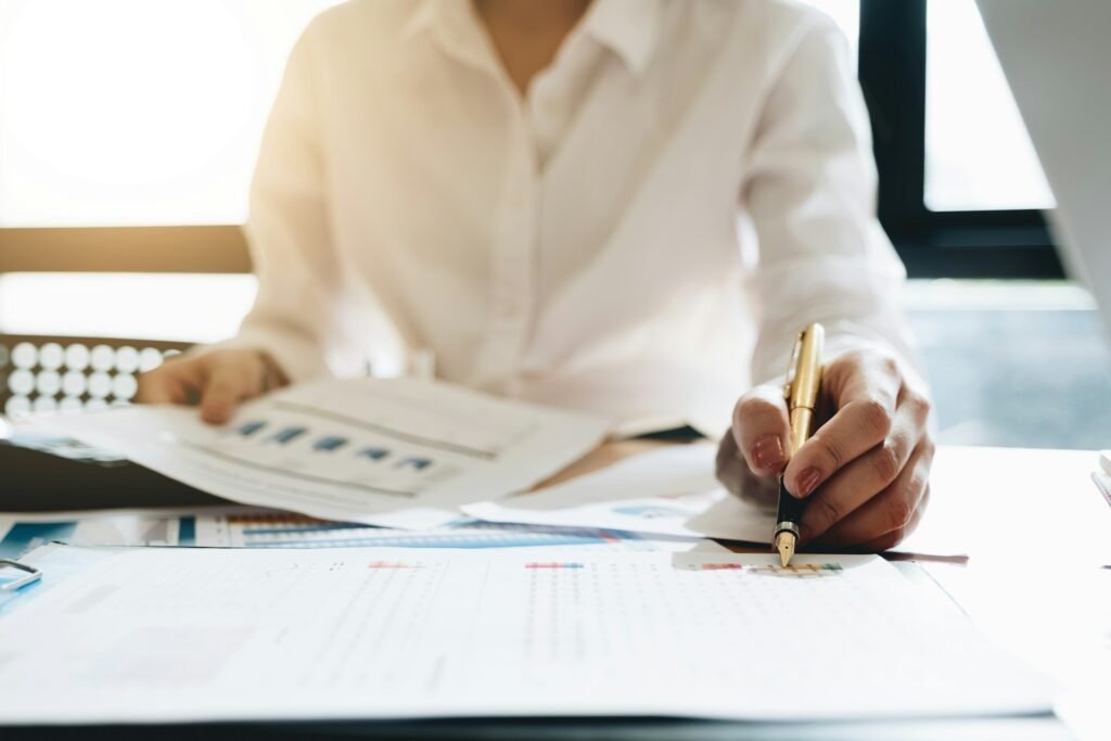 Freelancer reviewing printed financial reports and charts with a pen and bookkeeper software at an office desk.