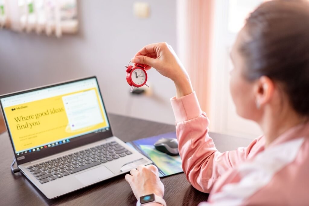 A freelancer working at a laptop with an alarm clock on the desk, tracking time against a deadline.