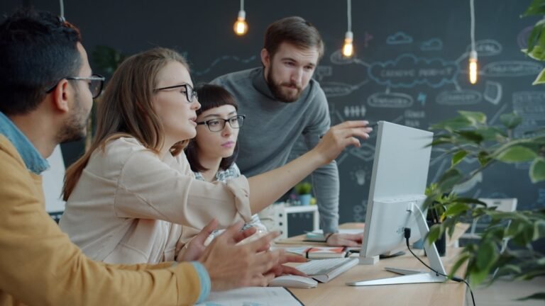 A group of colleagues collaborating and pointing at a laptop screen in an open-plan office. They are utilizing some of the best tools for managing freelance teams.