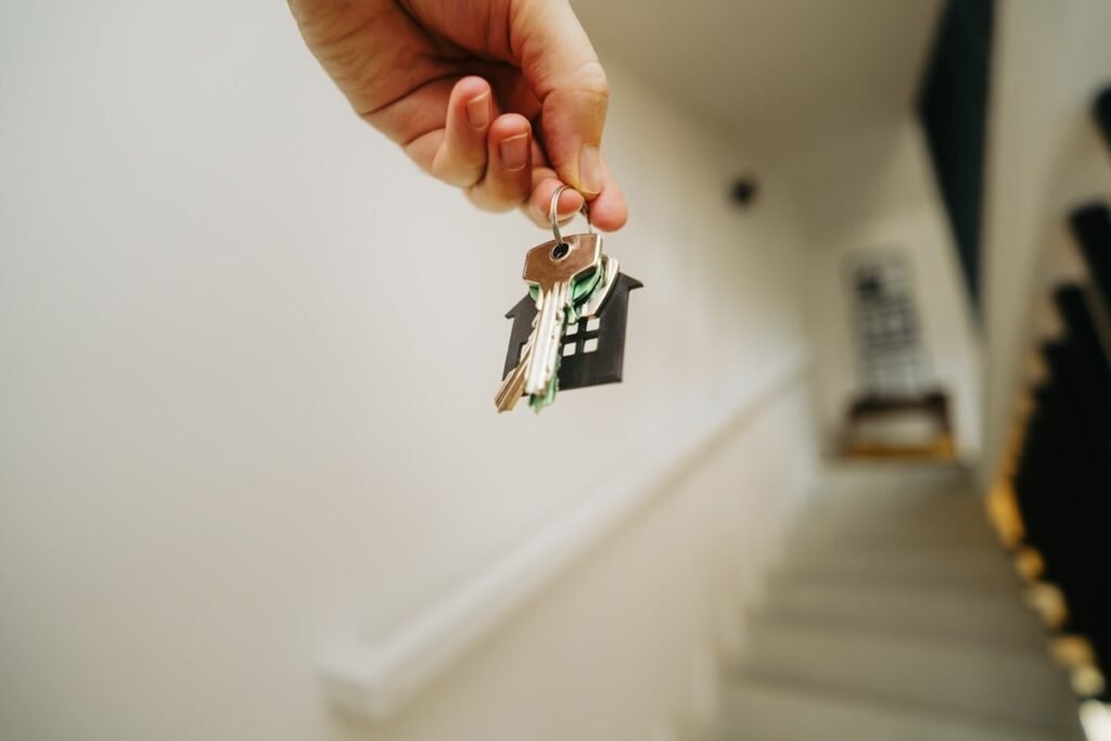 A hand holding a set of keys in front of a new house.