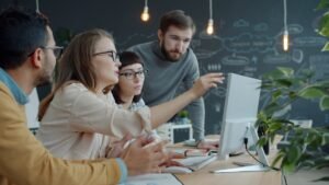A group of colleagues collaborating and pointing at a laptop screen in an open-plan office. They are utilizing some of the best tools for managing freelance teams.