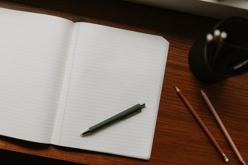 An open blank notebook with a pen and pencils on a wooden desk, ready for a brain dump of tasks.