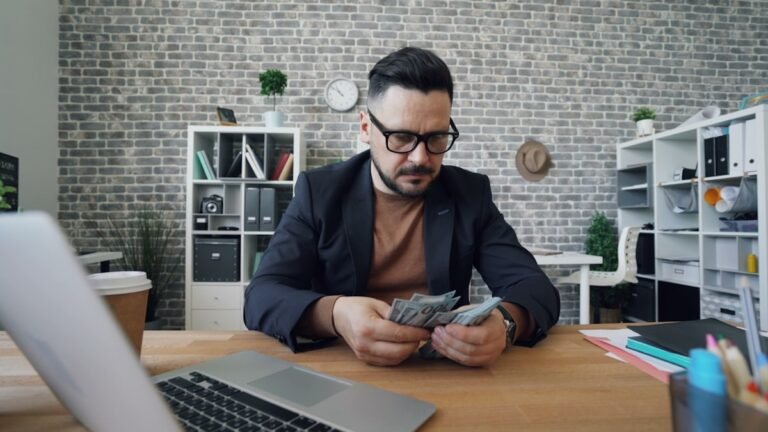 A man sitting at a desk counting dollar bills while learning how to manage finances as a freelancer.