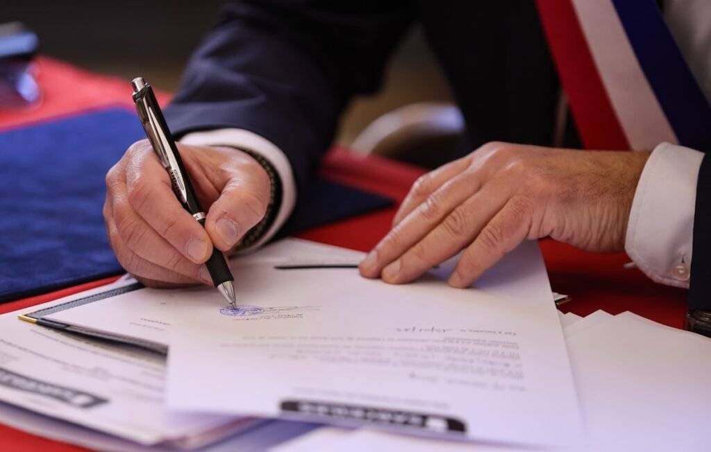A person signing a contract document with a pen at a desk.