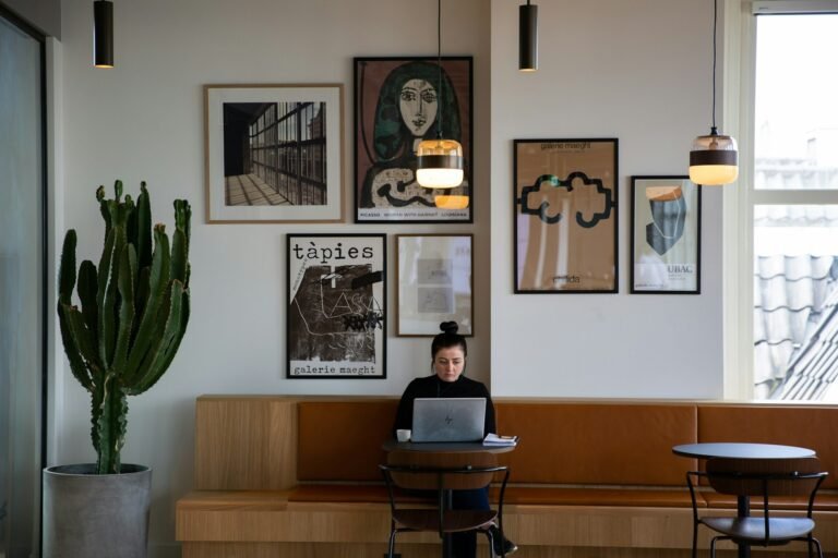Remote worker on a laptop at a café table beneath framed gallery art prints, looking for the best tools for tracking freelance contracts and expenses