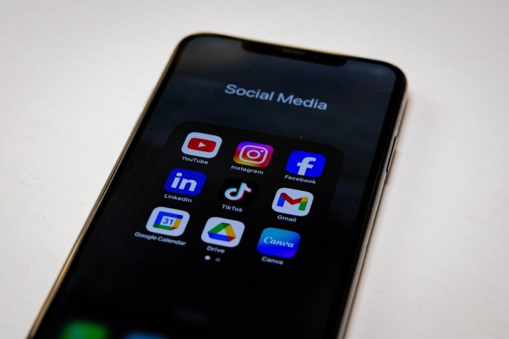 A close-up of a smartphone screen showing a folder of social media apps, including Instagram, Facebook, LinkedIn, TikTok, and YouTube.