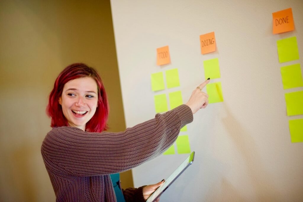 A person in a grey sweater arranging white and yellow sticky notes on a kanban board.