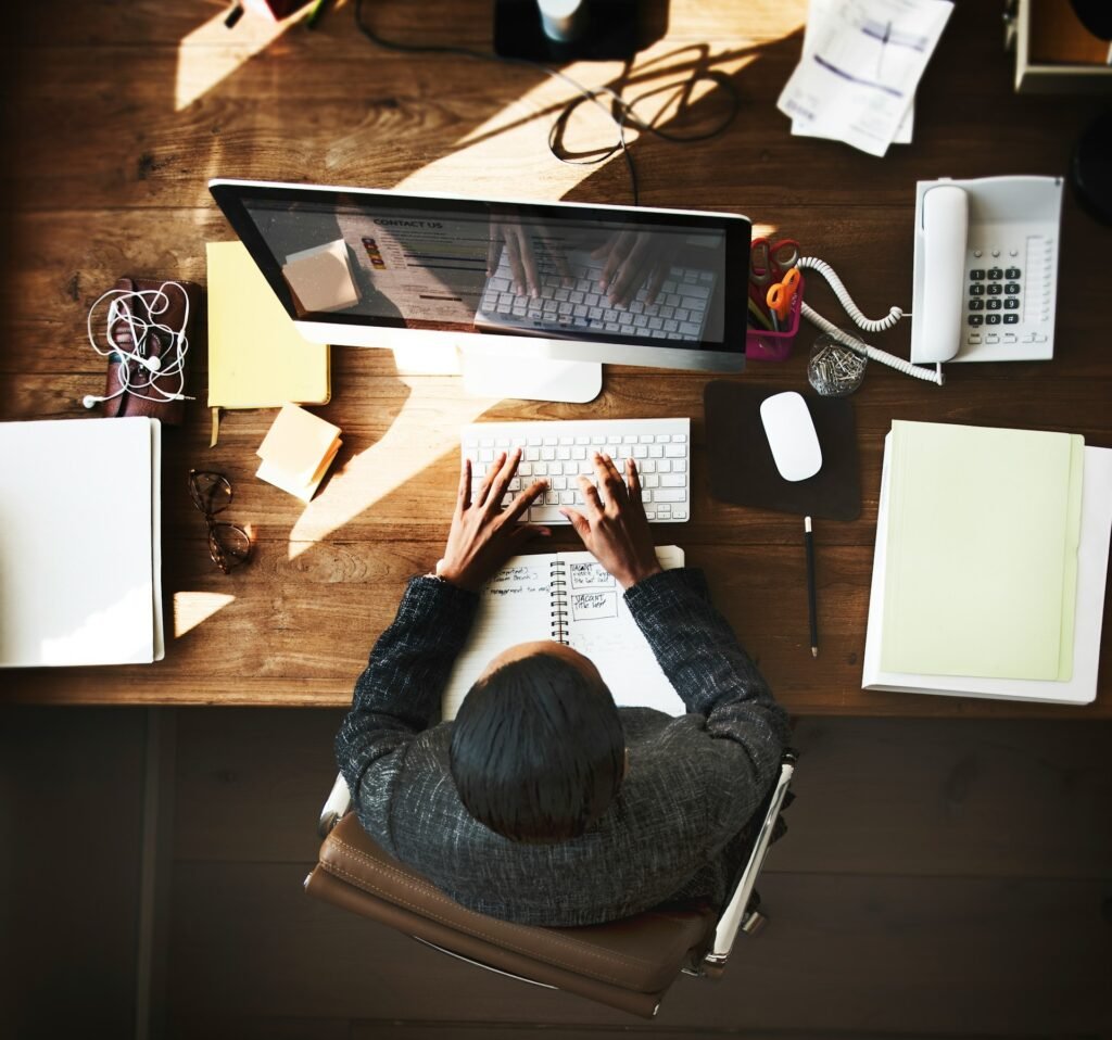 A top-down view of a freelancer working at a computer, wooden desk, notebooks open