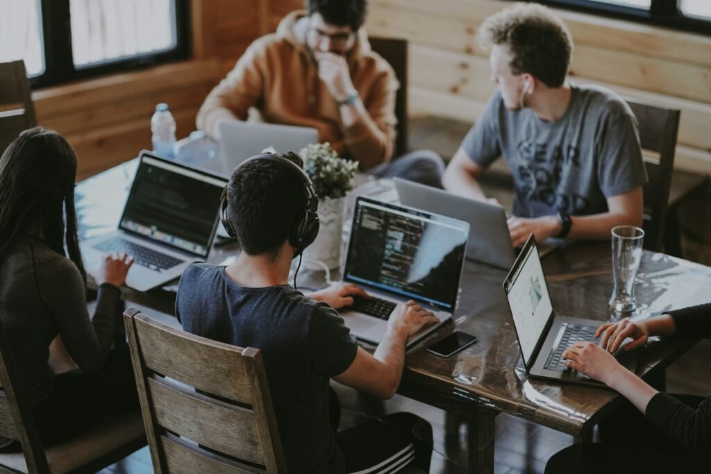 A young team of freelancers sits working on laptops around a wooden desk
