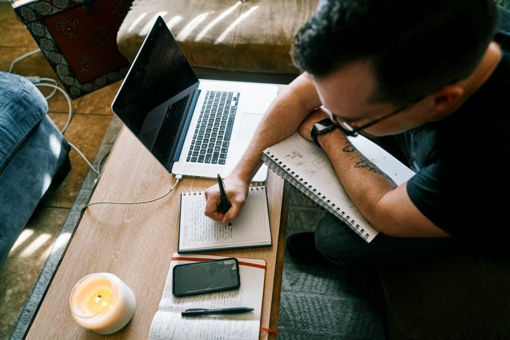 Freelancer in a black t-shirt writing on paper at a desk, working out why he's busy but always broke due to cash flow problems