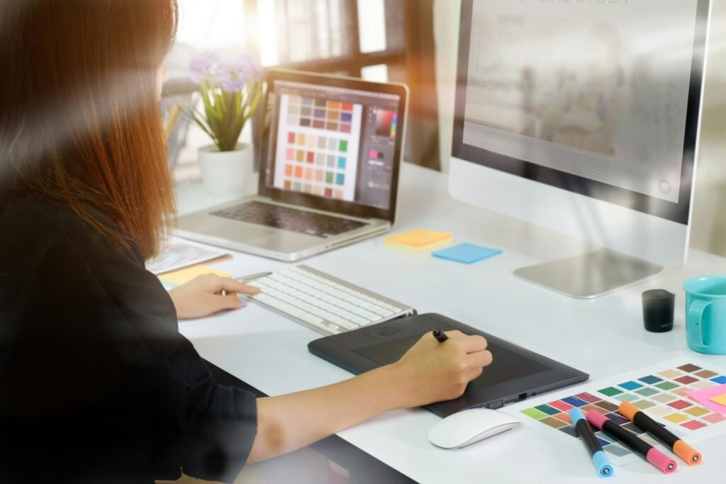 Freelance graphic designer working on a computer and tablet with creative and writing apps