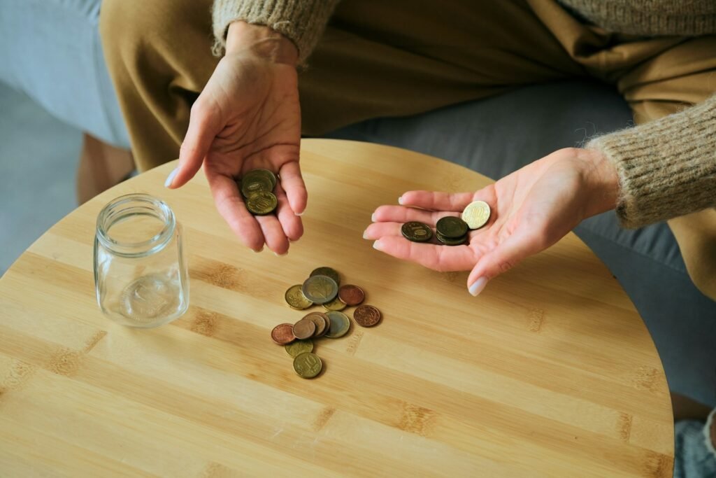 Hands counting coins beside a glass savings jar, illustrating a freelancer building a cash reserve