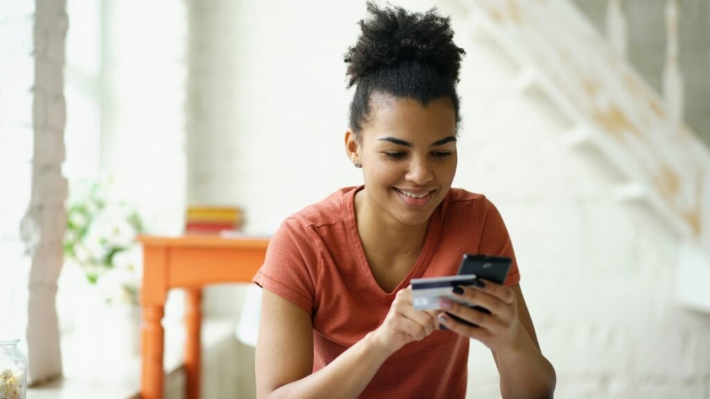 Freelancer smiling while holding a credit card and phone, checking a bank account comparison site