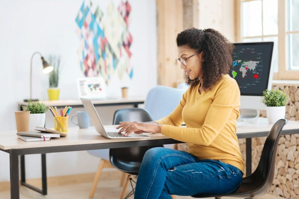 Freelancer smiling while working on a laptop at a table, planning her monthly cash flow using a cash flow projection template