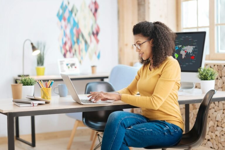 Freelancer smiling while working on a laptop at a table, planning her monthly cash flow using a cash flow projection template