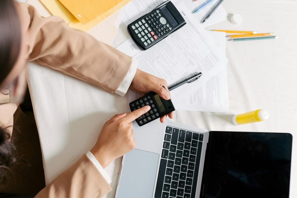 Freelancer reviewing her cash flow projection with a calculator and laptop during a monthly check-in