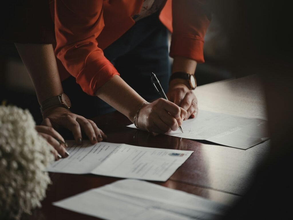 Freelancer in an orange shirt signing paperwork, the manual version of an e-signature app
