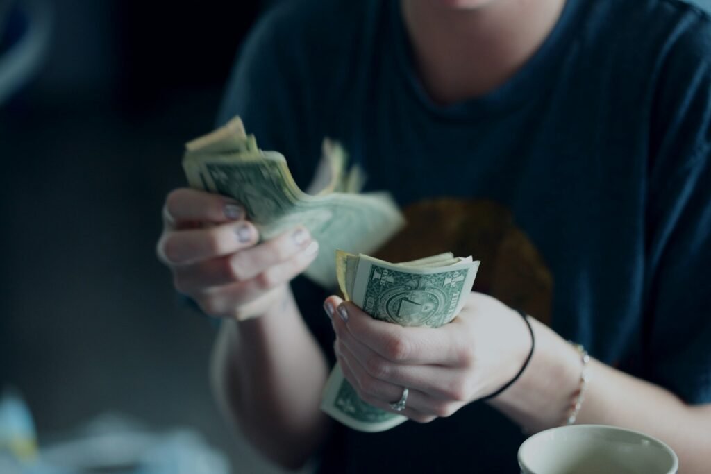 Hands counting US dollar banknotes, showing the gap between a freelancer's paper profit and cash in the bank