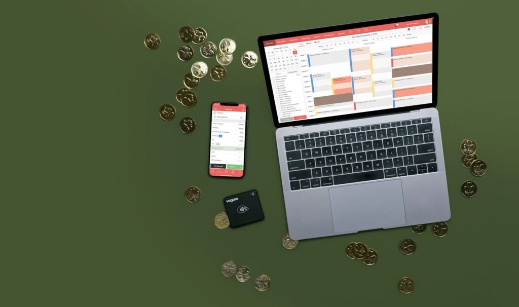 A laptop set up with timeblocking on the screen, and smartphone, a card reader next to it and coins scattered around, aesthetic green background