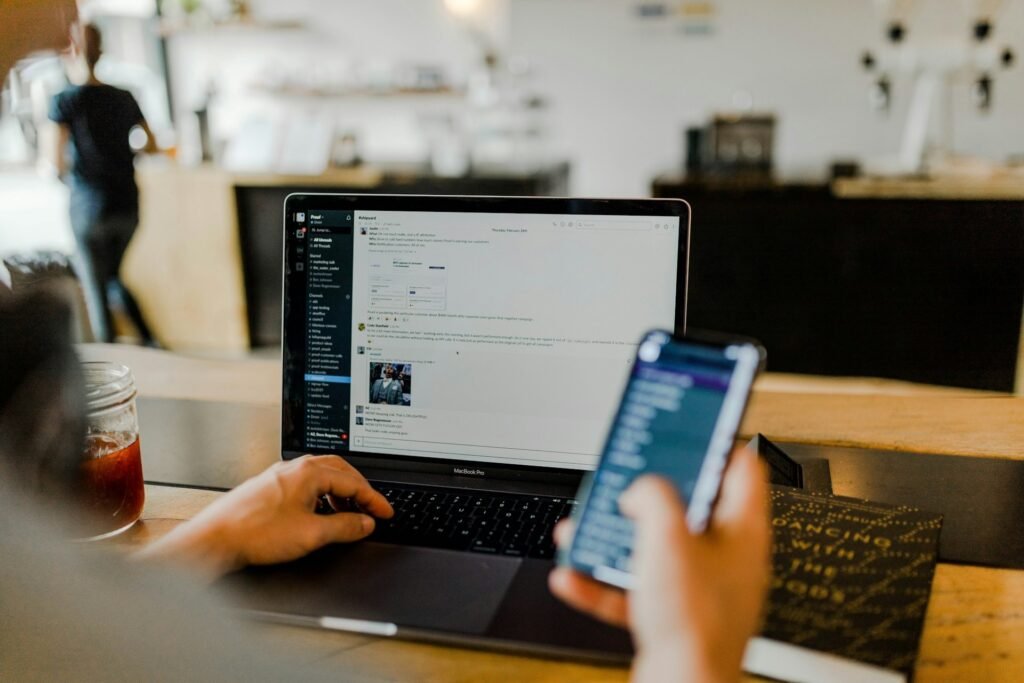 Freelancer using a phone and laptop together to message clients and schedule calls