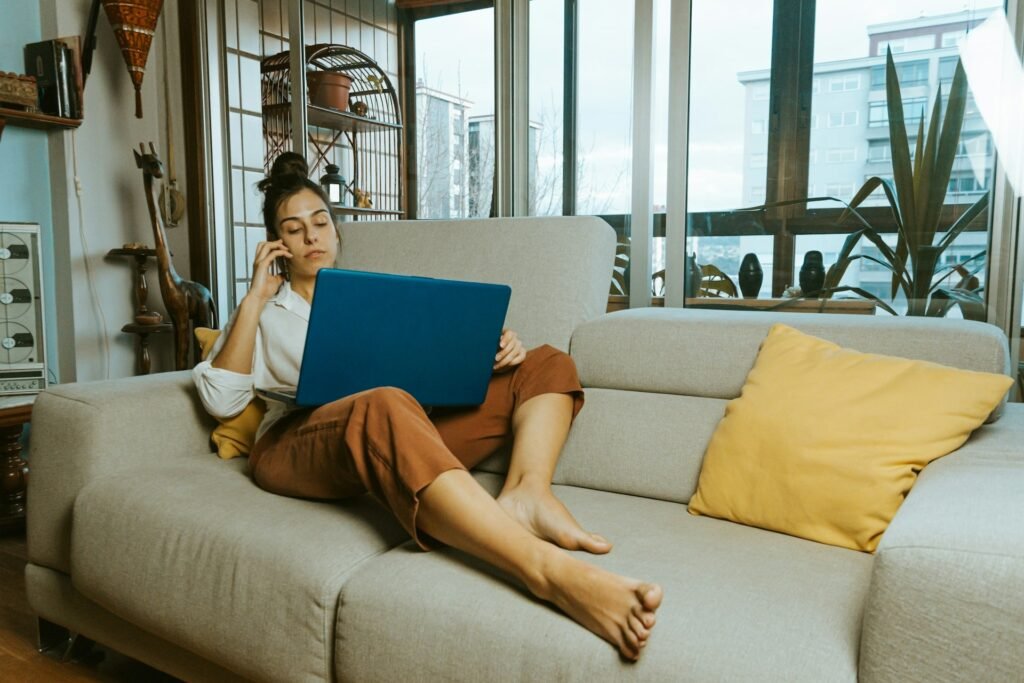 Freelancer reclining on a sofa taking a client call with a laptop, illustrating the timing gap behind cash flow problems