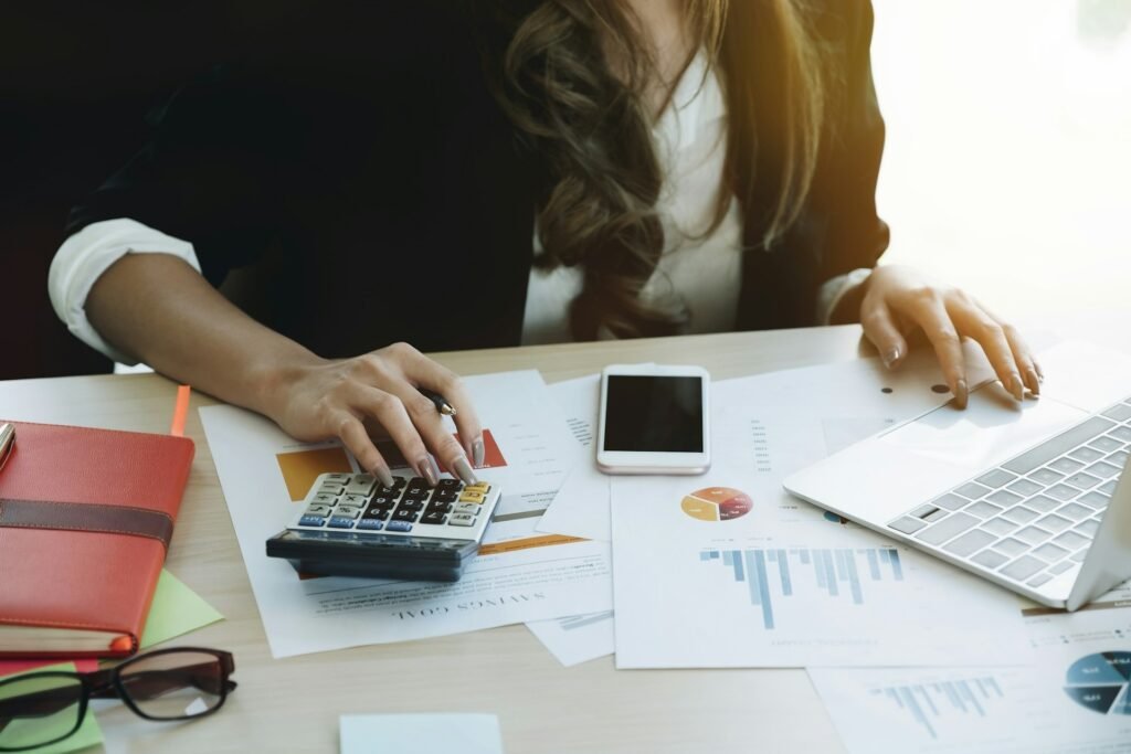 Freelancer using a calculator and laptop to track expenses and tax with an accounting app