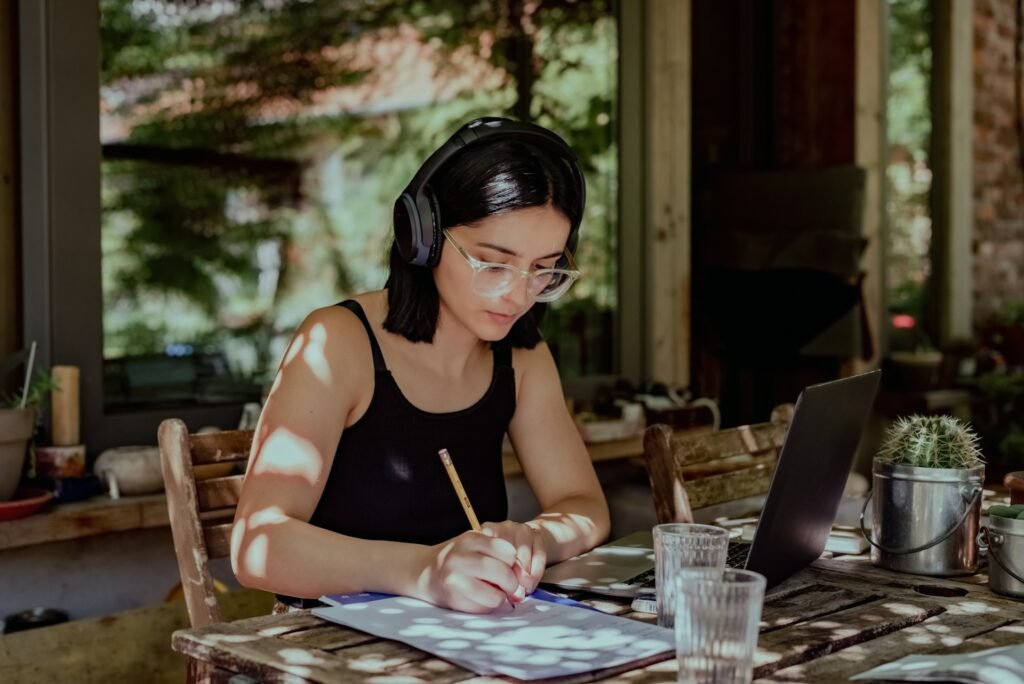 Freelancer filling out a note taking template at a sunlit table with a laptop open beside her