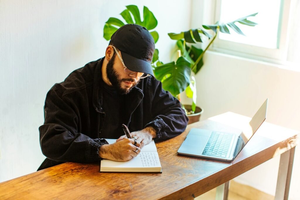 Freelancer taking handwritten notes in a notebook at a desk with a laptop