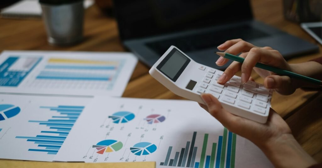 Freelancer using a calculator and laptop to reconcile monthly bookkeeping records