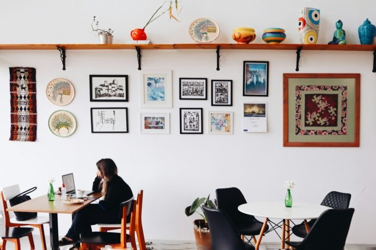 Freelancer working on a laptop at a café table with a gallery wall behind