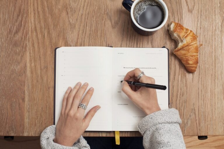 Hands filling in a Full Focus Planner spread with goals and targets beside coffee