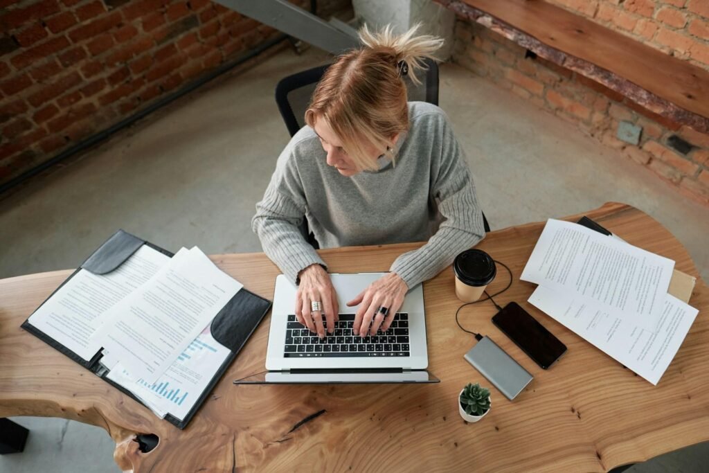 Overhead view of a laptop on a wooden desk surrounded by paper envelopes
