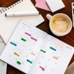 Paper planner with colour-coded entries across the month, beside a laptop and coffee